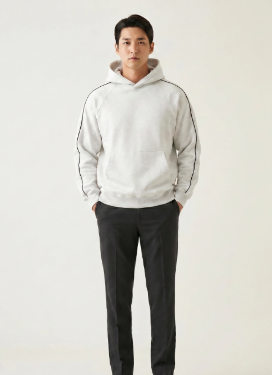 Man wearing a light gray hoodie and dark pants on a plain background