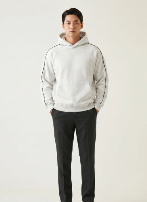 Man wearing a light gray hoodie and dark pants on a plain background